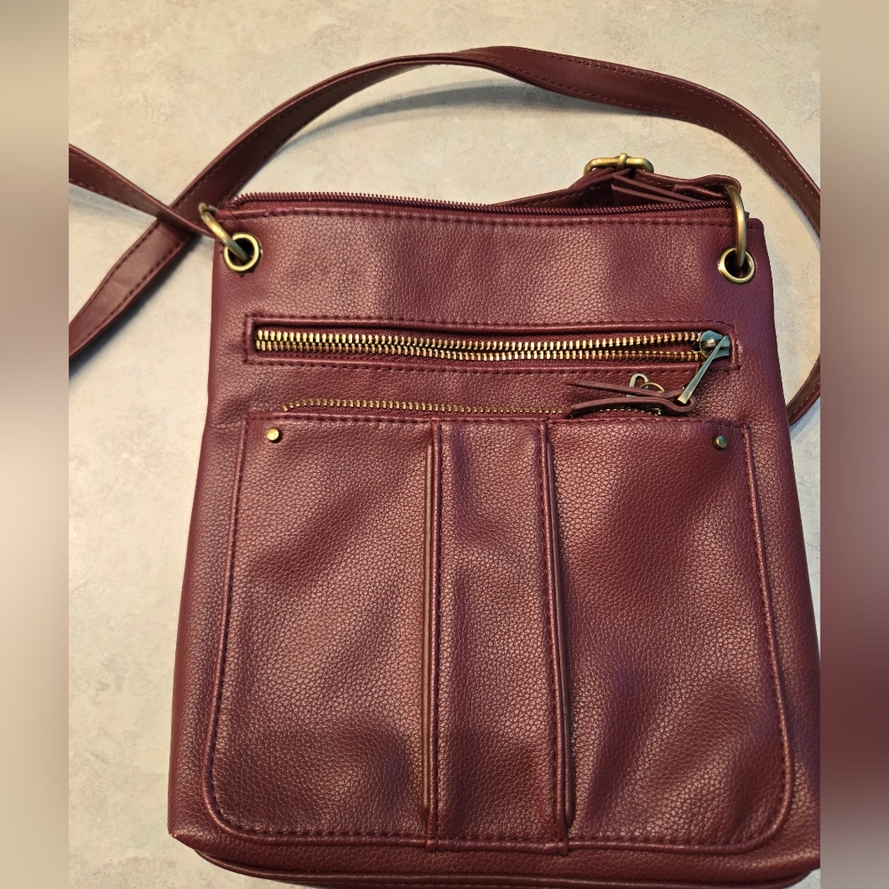 Small burgundy cross body purse with several zipper pockets.
